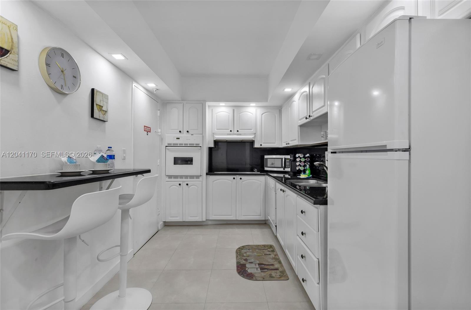 A white kitchen features black countertops, white cabinetry, a breakfast bar, and tile flooring — 3901 S Ocean Dr # 8C, Hollywood FL 33019, HOLLYWOOD, FL