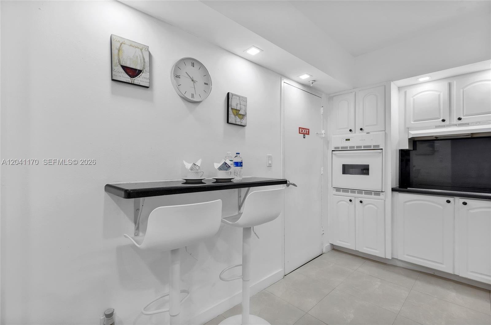 A kitchen features white cabinetry, a black countertop, and a wall-mounted breakfast bar with stools — 3901 S Ocean Dr # 8C, Hollywood FL 33019, HOLLYWOOD, FL