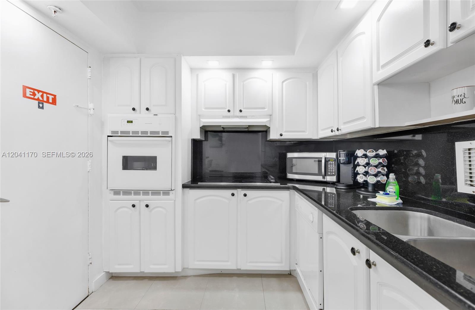 A kitchen features white cabinets, black countertops, a wall oven, and a stainless steel sink — 3901 S Ocean Dr # 8C, Hollywood FL 33019, HOLLYWOOD, FL