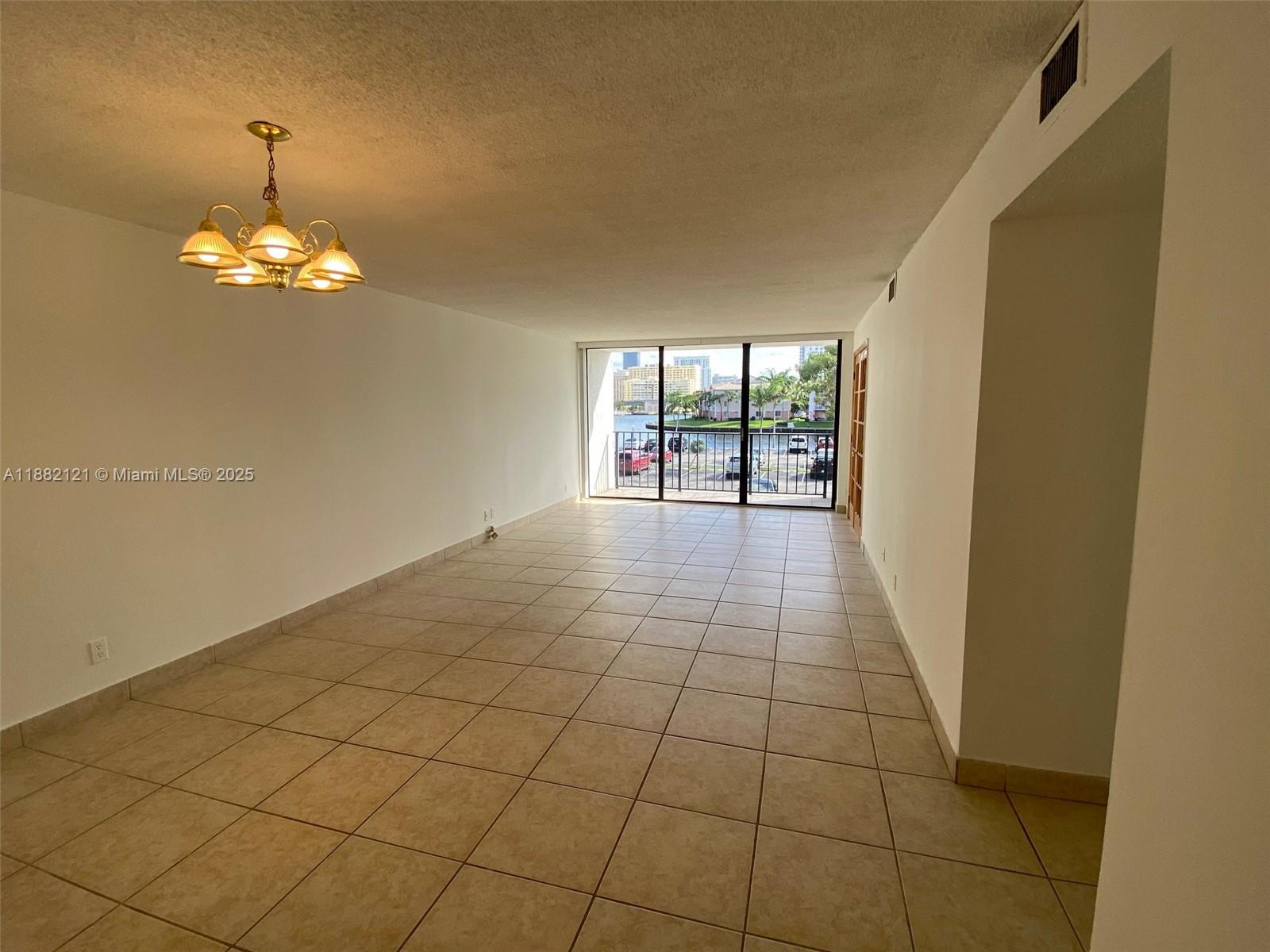 An empty room features beige tile flooring, a chandelier, and a balcony with water views — 200 Leslie Dr # 228, Hallandale Beach FL 33009, HALLANDALE BEACH, FL