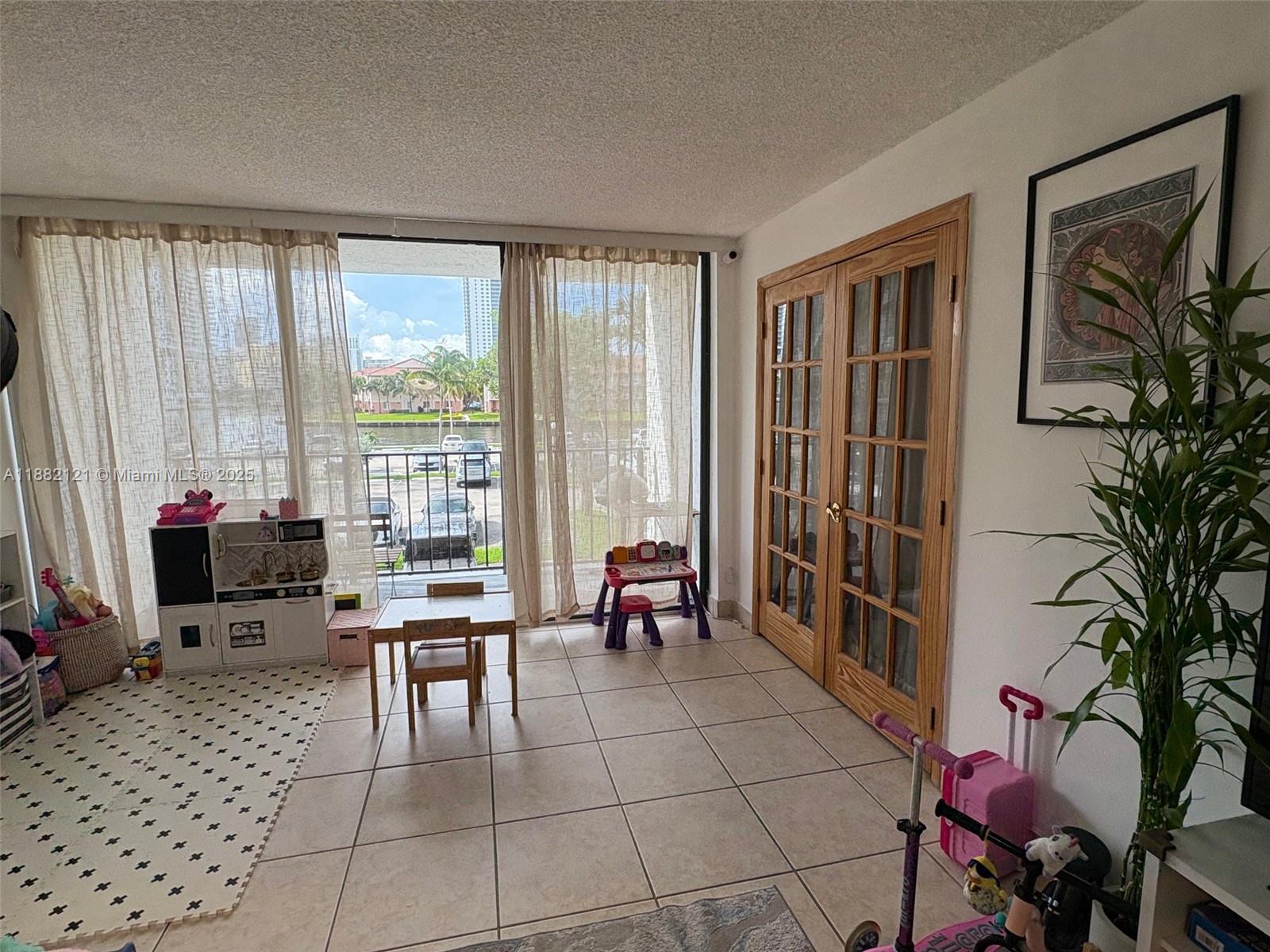 A sunlit playroom features tile flooring, French doors, and a balcony overlooking a parking lot — 200 Leslie Dr # 228, Hallandale Beach FL 33009, HALLANDALE BEACH, FL