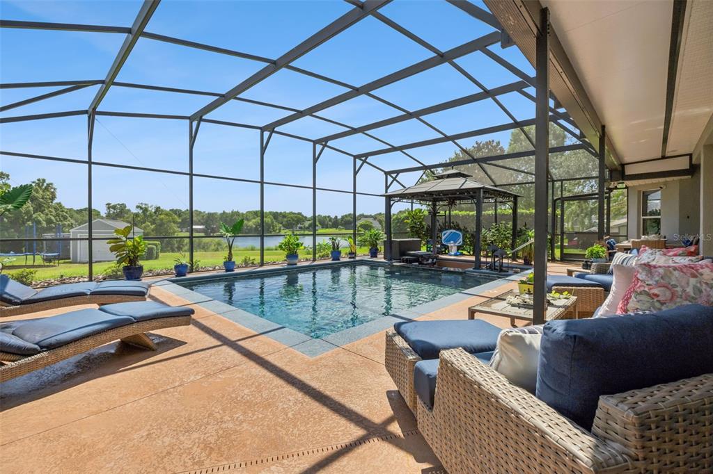 A screened-in patio features a rectangular swimming pool, lounge chairs, and a view of a lake — 7648 LAKE ANGELINA DRIVE, MOUNT DORA, FL