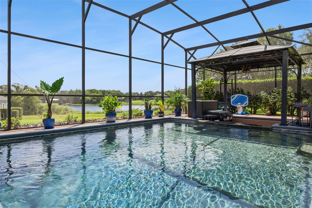 A screened-in swimming pool area features a gazebo, potted plants, and a lake view — 7648 LAKE ANGELINA DRIVE, MOUNT DORA, FL