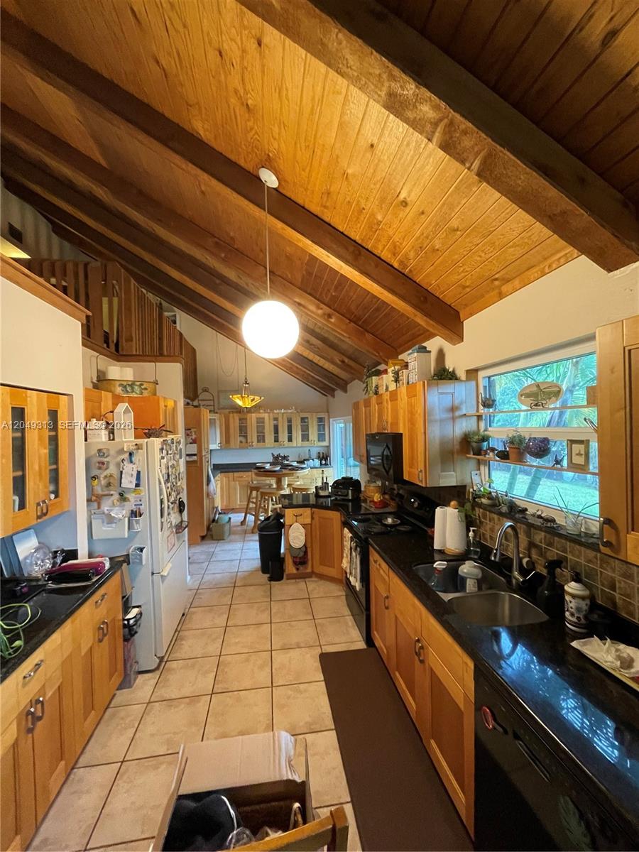 A kitchen features wood cabinets, black countertops, tile flooring, and a vaulted wood-paneled ceiling — 2811 Devonwood Ave, Miramar FL 33025, MIRAMAR, FL