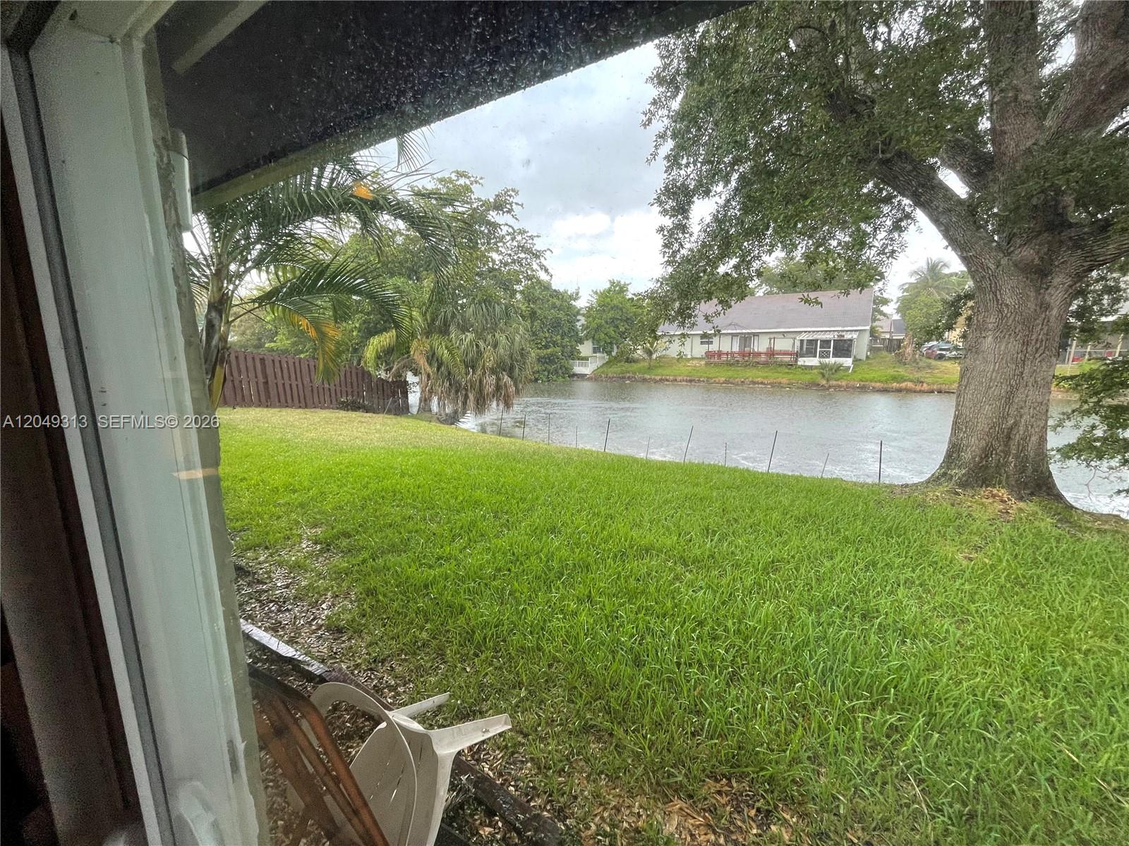 A view from a window shows a grassy backyard leading to a canal and trees — 2811 Devonwood Ave, Miramar FL 33025, MIRAMAR, FL