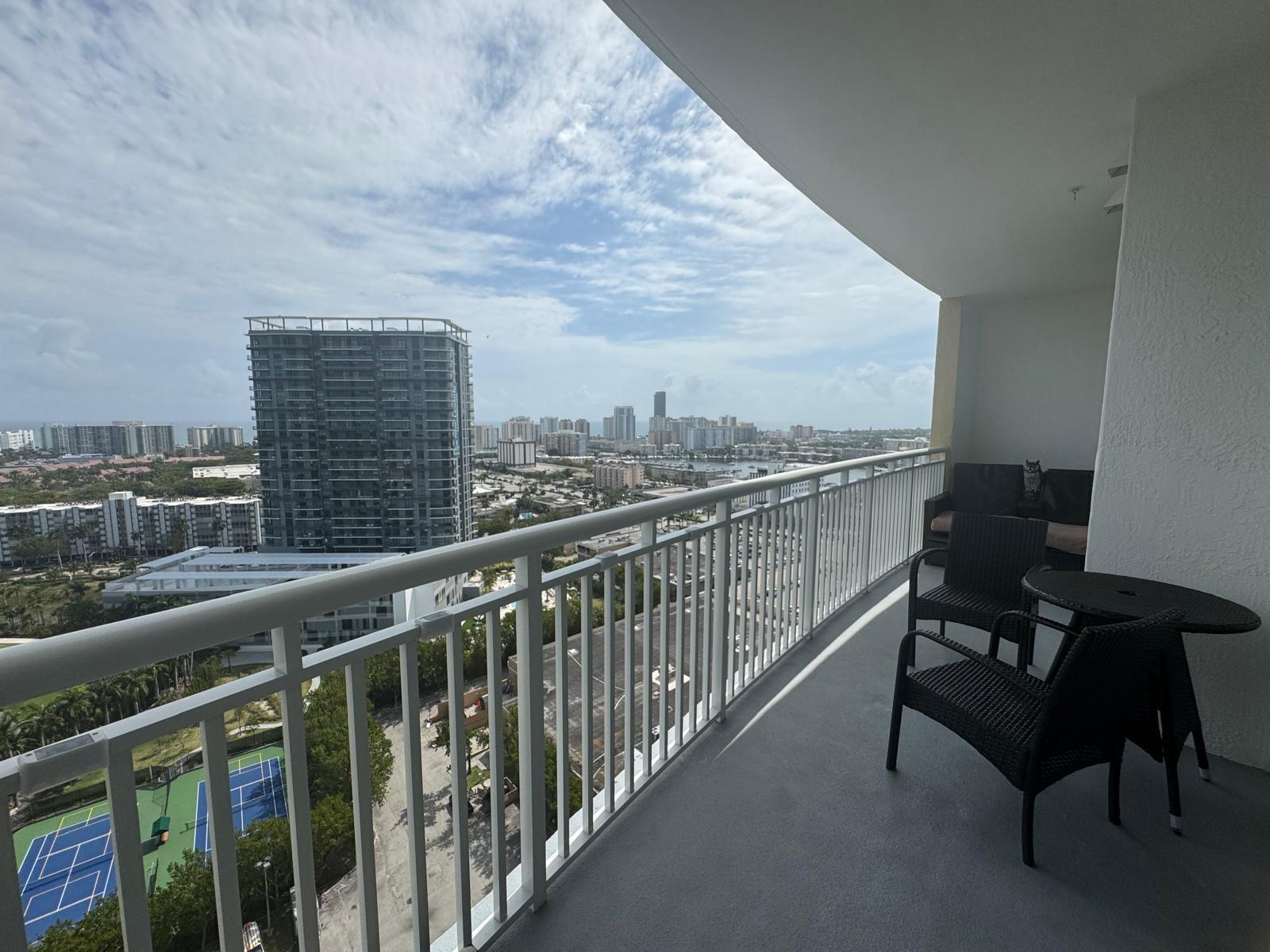 A balcony with outdoor furniture overlooks a city skyline, a tennis court, and high-rise buildings — 1755 E Hallandale Beach Boulevard # 2104e, FL 33009, FL