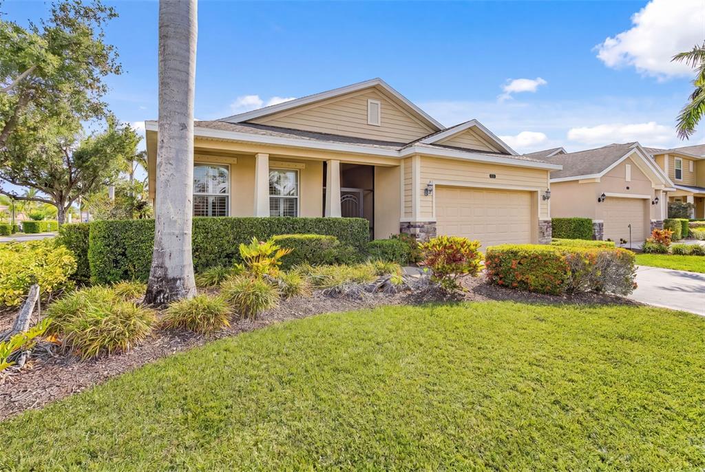 A single-story house with tan siding, a two-car garage, and manicured landscaping — 8531 KARPEAL DRIVE, SARASOTA, FL