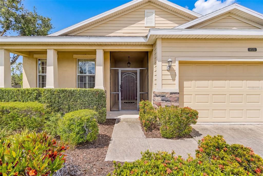 The exterior of a single-story house features a beige facade, a garage, and a screened entryway — 8531 KARPEAL DRIVE, SARASOTA, FL
