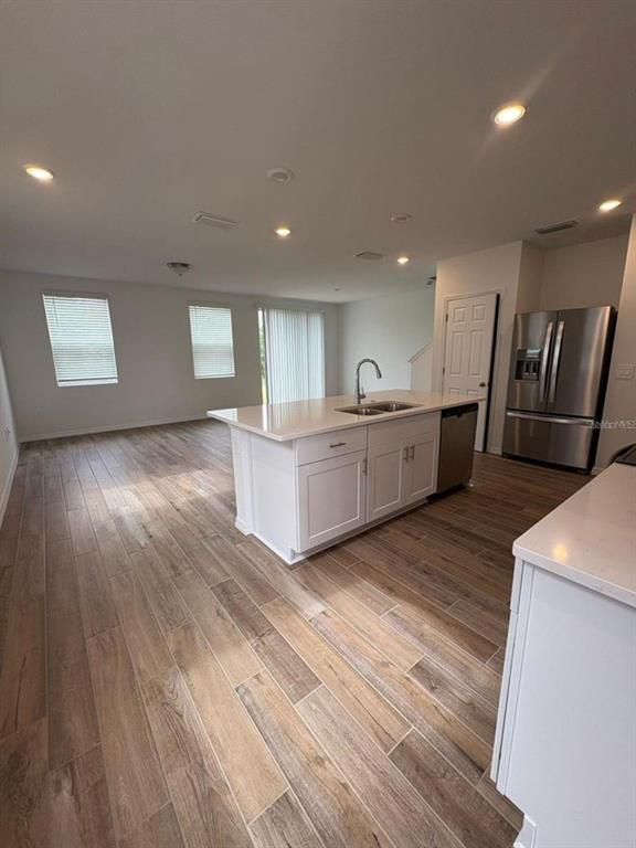 An open-concept kitchen features a white island, stainless steel appliances, and wood-look tile flooring — 16407 BIRD OF PARADISE AVENUE, CLERMONT, FL
