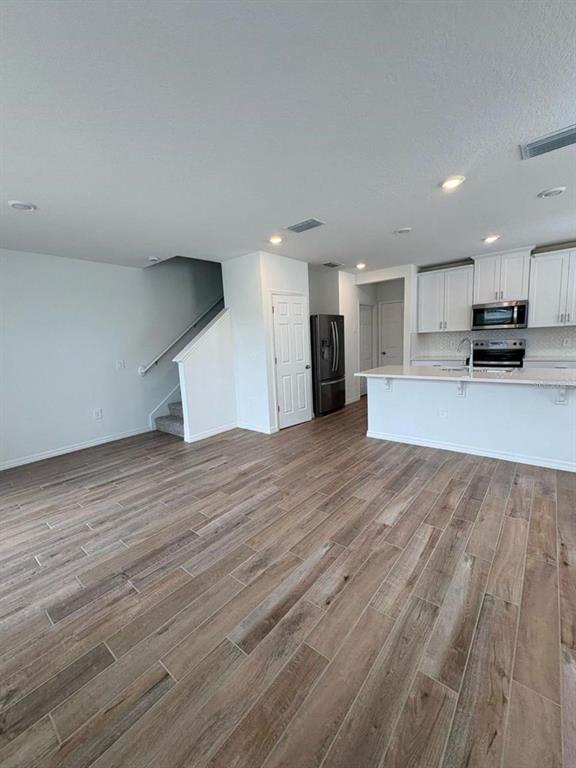 An open-concept kitchen and living area features wood-look tile flooring and a staircase — 16407 BIRD OF PARADISE AVENUE, CLERMONT, FL