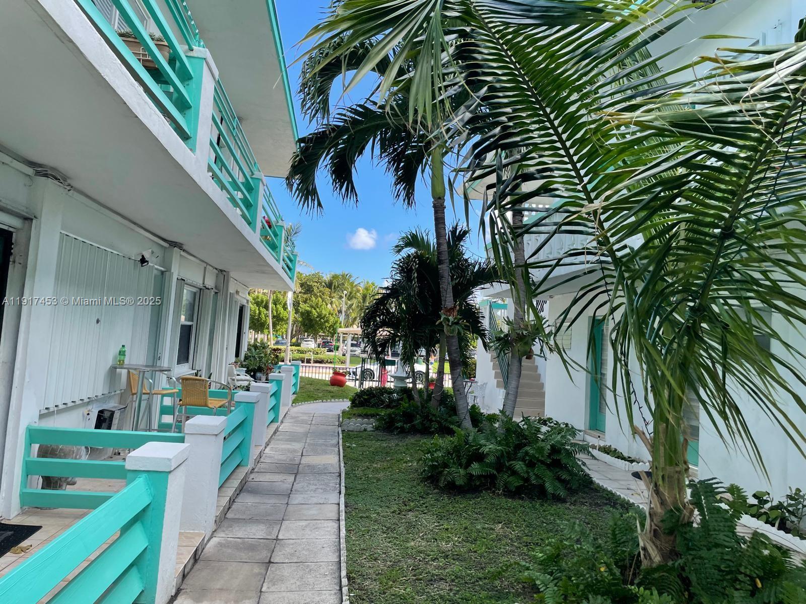 A paved walkway leads between two white buildings with turquoise railings and palm trees — 6490 Collins Ave # 5, Miami Beach FL 33141, MIAMI BEACH, FL