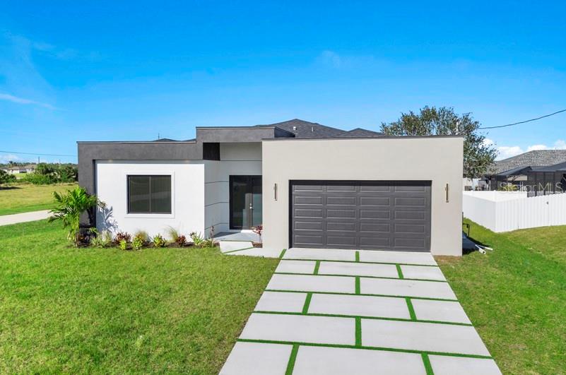 A modern single-story house with a flat roof, white and gray exterior, and a paver driveway — 3927 NW 38TH STREET, CAPE CORAL, FL