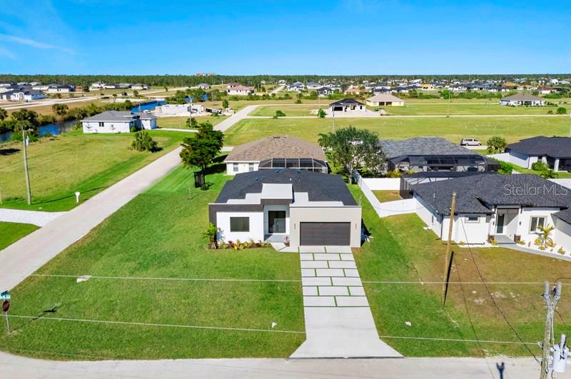 An aerial view shows a modern single-story house with a paved driveway and surrounding neighborhood — 3927 NW 38TH STREET, CAPE CORAL, FL