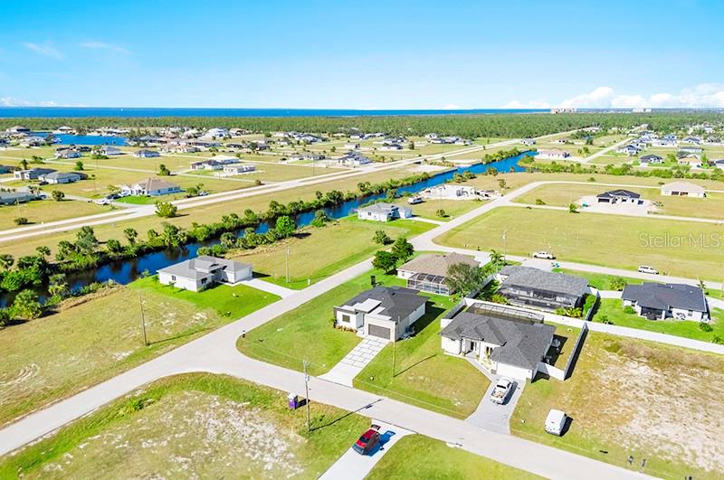 An aerial view shows suburban houses near a canal with the ocean in the distance — 3927 NW 38TH STREET, CAPE CORAL, FL