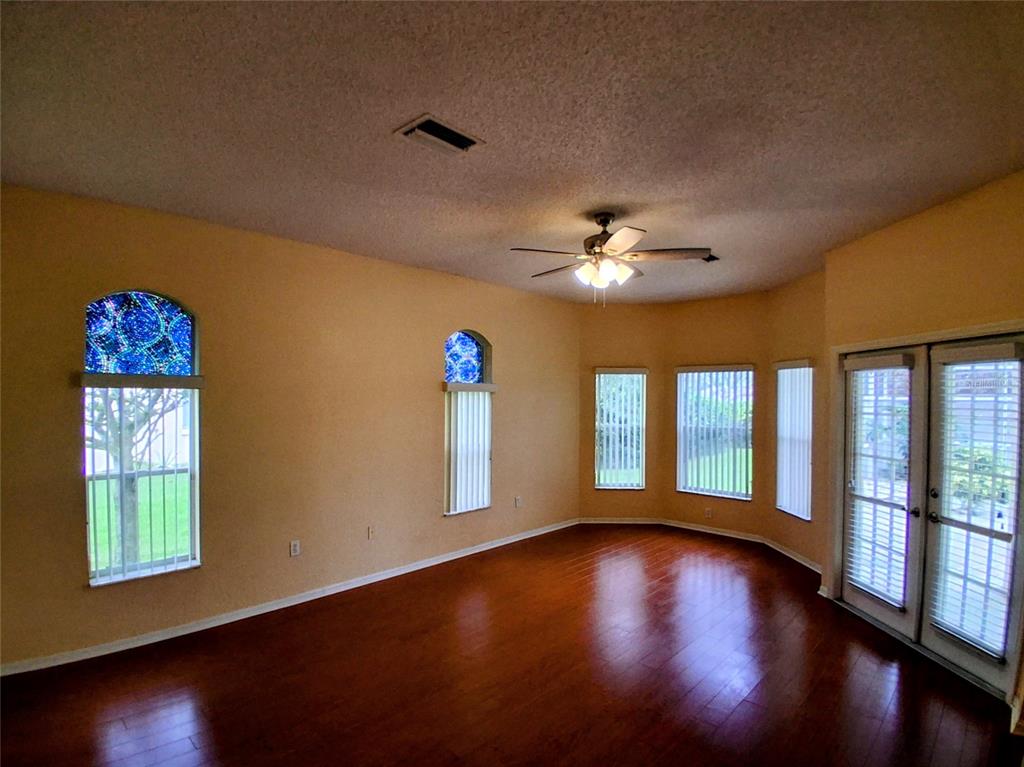 An empty living room features hardwood floors, a ceiling fan, and several windows with blinds — 3392 ST IVES BOULEVARD, SPRING HILL, FL
