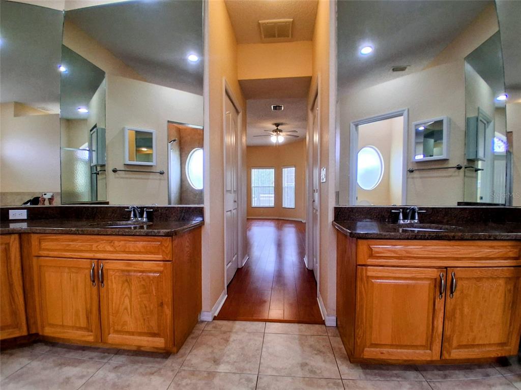 A bathroom with dual wood vanities, granite countertops, and a hallway leading to another room — 3392 ST IVES BOULEVARD, SPRING HILL, FL