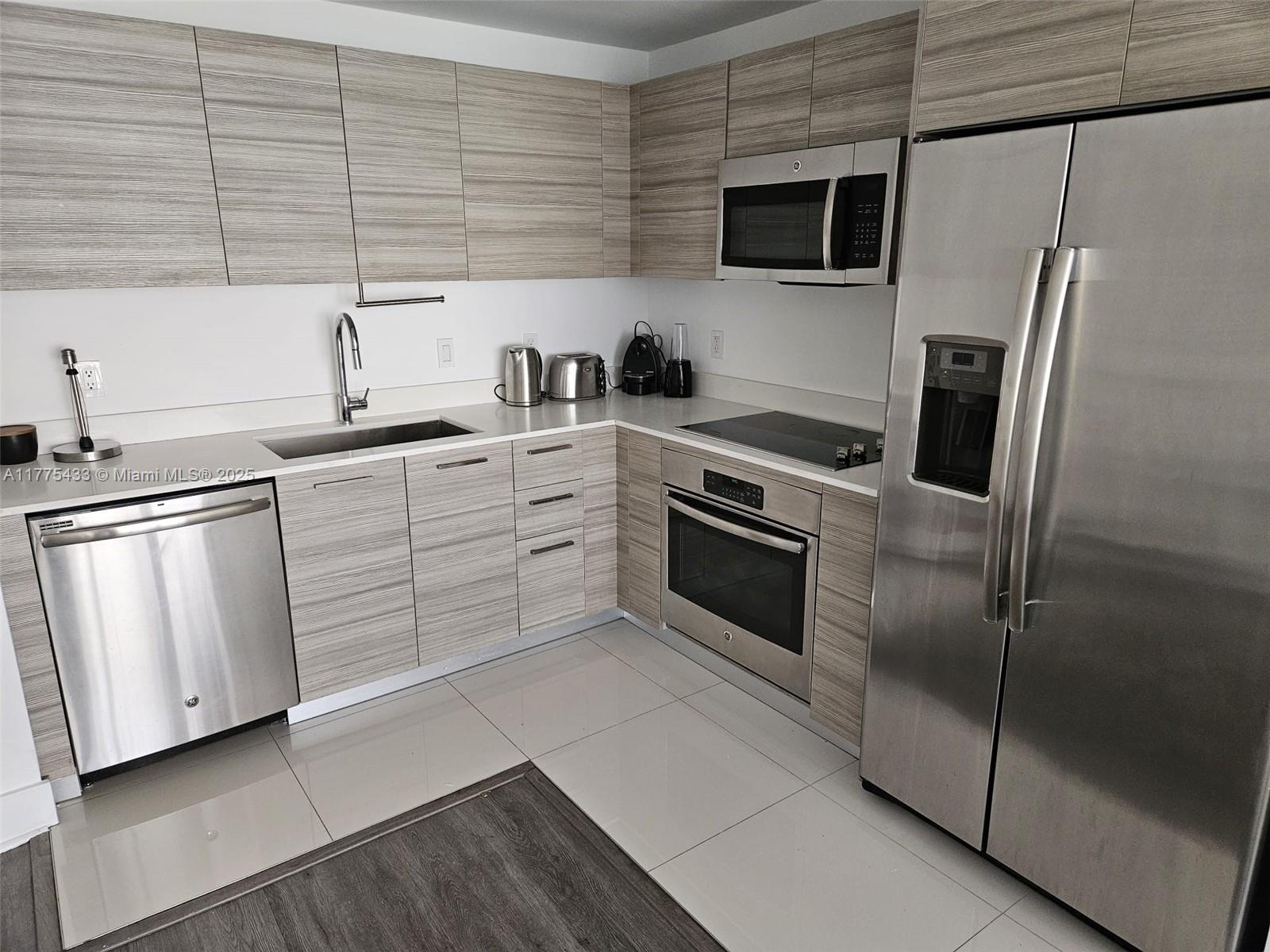 A modern kitchen features stainless steel appliances, light wood-grain cabinets, and light-colored tile flooring — 121 NE 34 ST # 2511, Miami FL 33137, MIAMI, FL