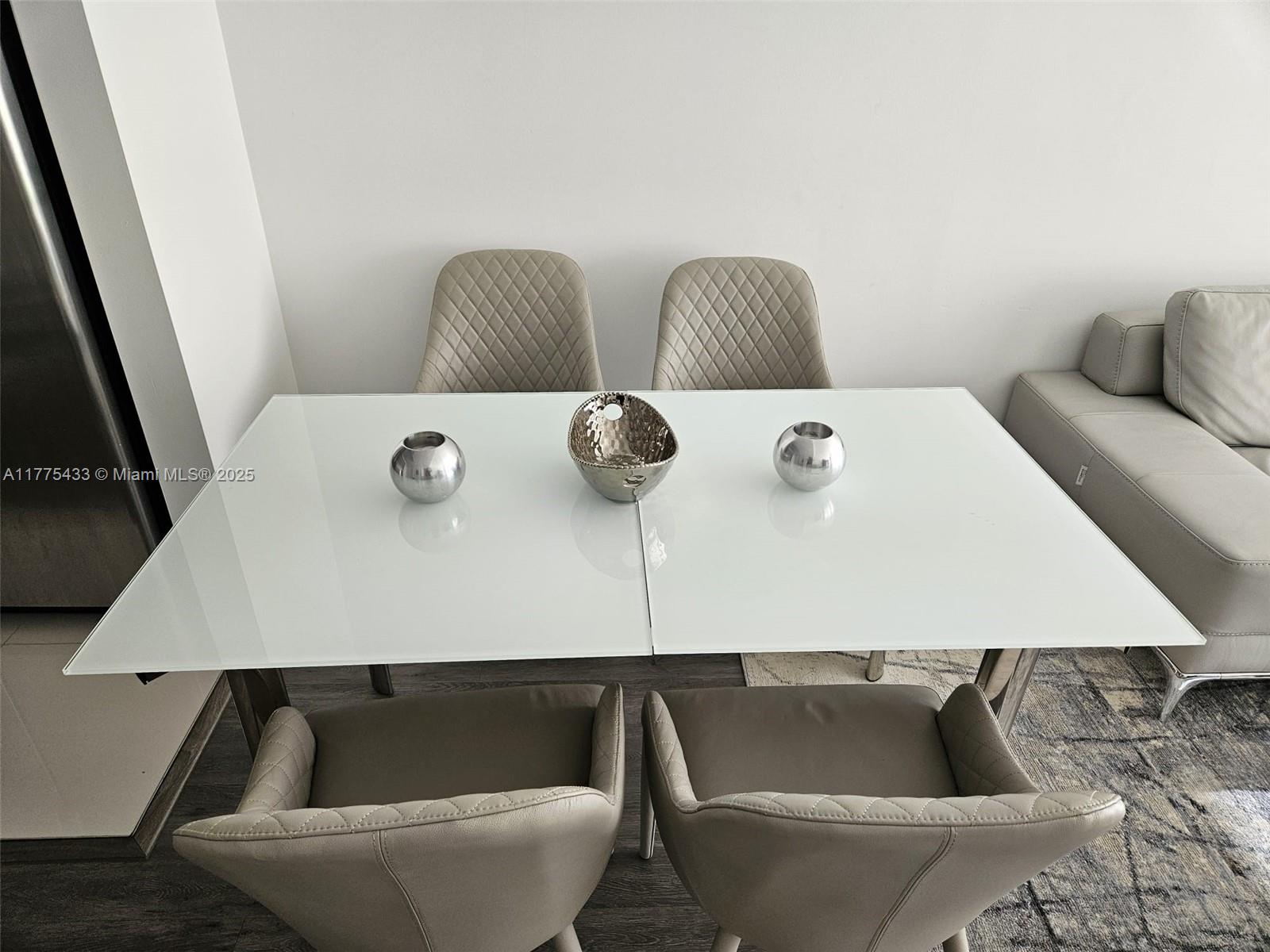 A dining area features a white glass table with four quilted chairs and decorative bowls — 121 NE 34 ST # 2511, Miami FL 33137, MIAMI, FL