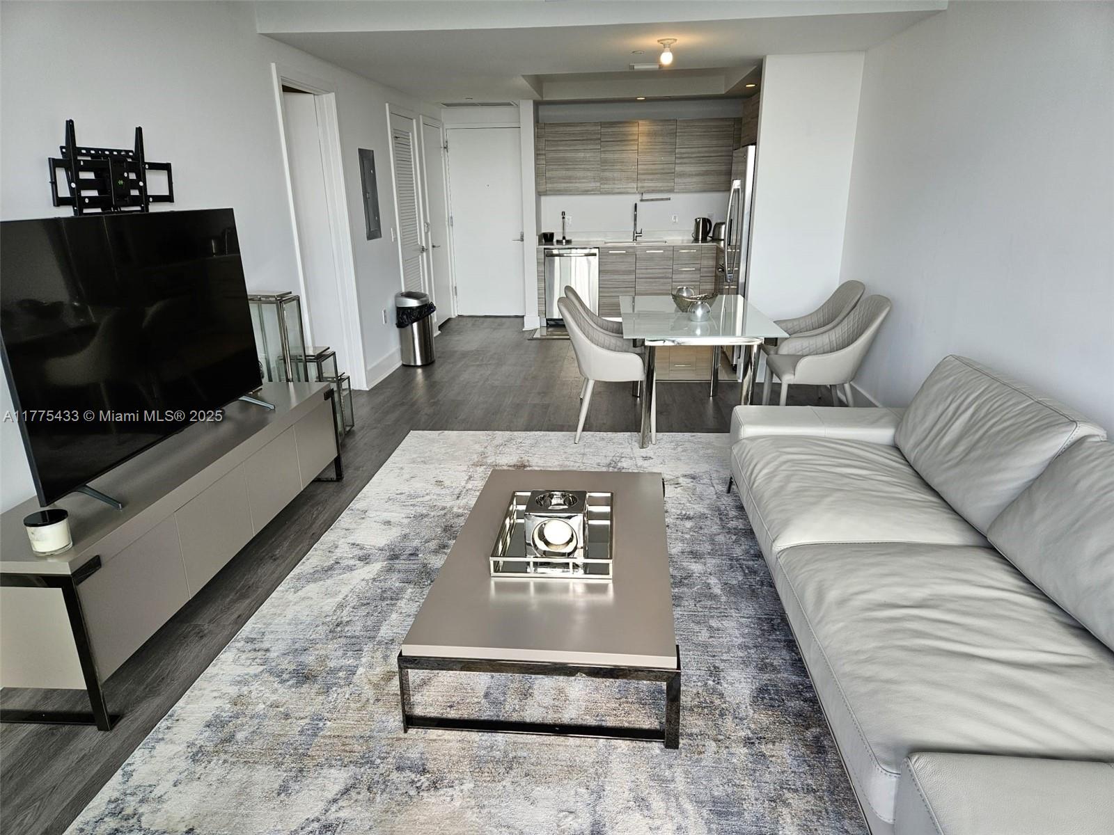 A modern living room features a grey sofa, coffee table, television, and an adjacent kitchen — 121 NE 34 ST # 2511, Miami FL 33137, MIAMI, FL