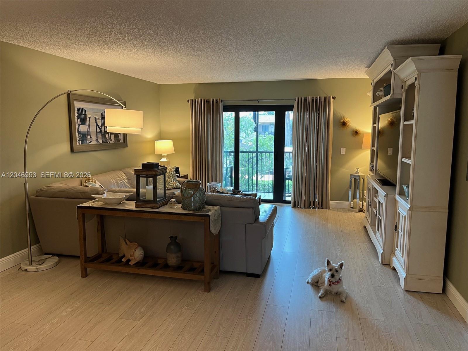 A living room features light wood flooring, sage green walls, a sofa, and a television unit — WESTON, FL