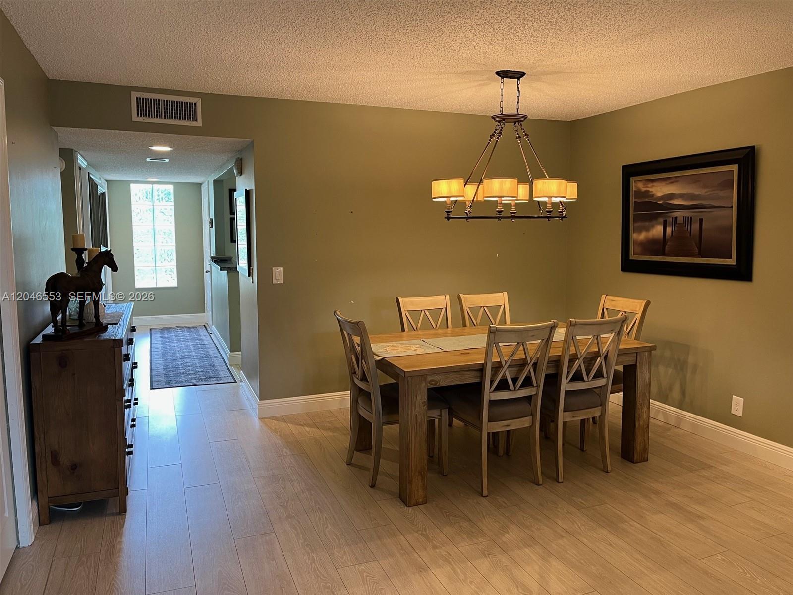 A dining room features a wooden table with six chairs, a chandelier, and light flooring — WESTON, FL