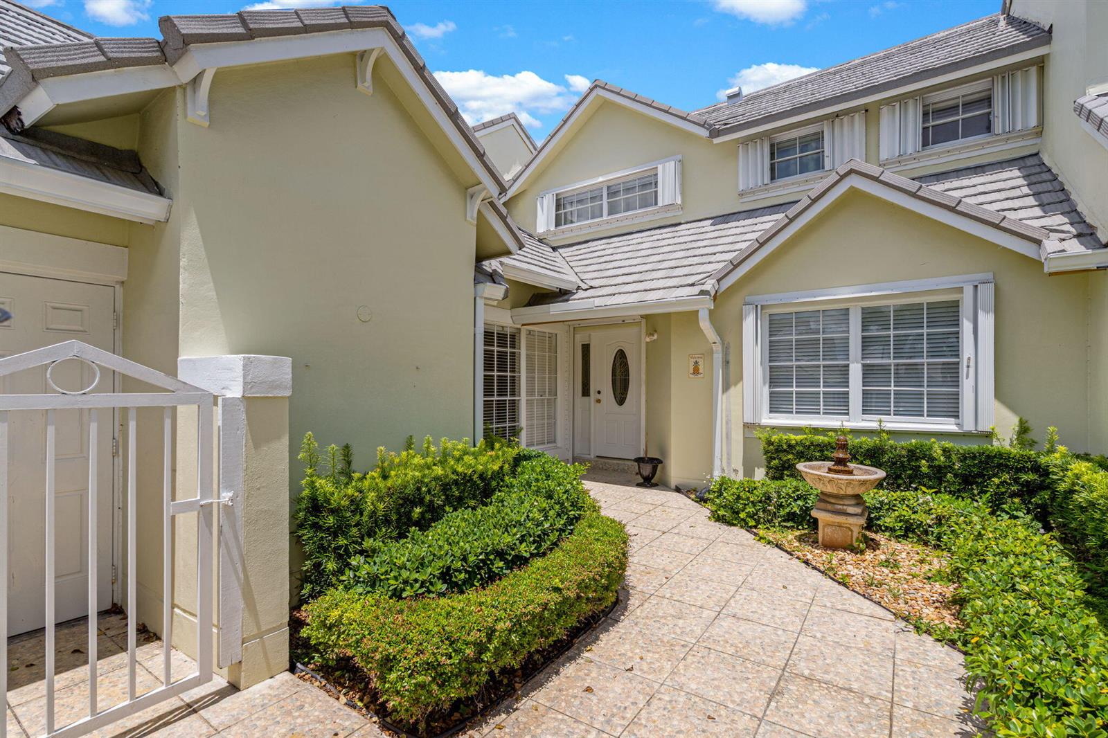 A paved walkway leads to the front entrance of a light-colored house with landscaping — 4825 NW 98th Place, Doral FL 33178, DORAL, FL