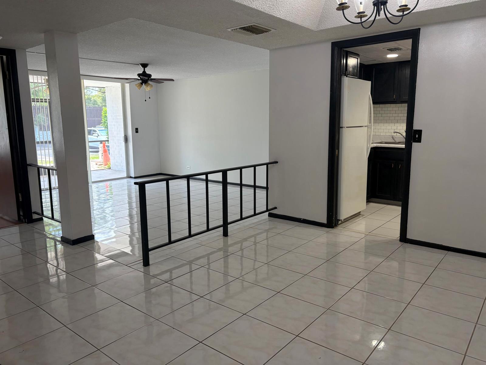A tiled living area features a black metal railing, a ceiling fan, and a kitchen doorway — 3660 Inverrary Drive # 1b, Lauderhill FL 33319, LAUDERHILL, FL