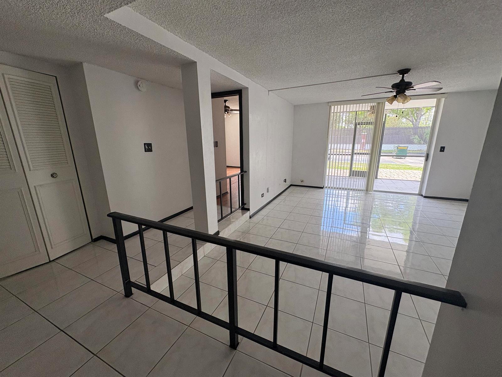 A living area with white tile floors, a black metal railing, and a sliding glass door — 3660 Inverrary Drive # 1b, Lauderhill FL 33319, LAUDERHILL, FL