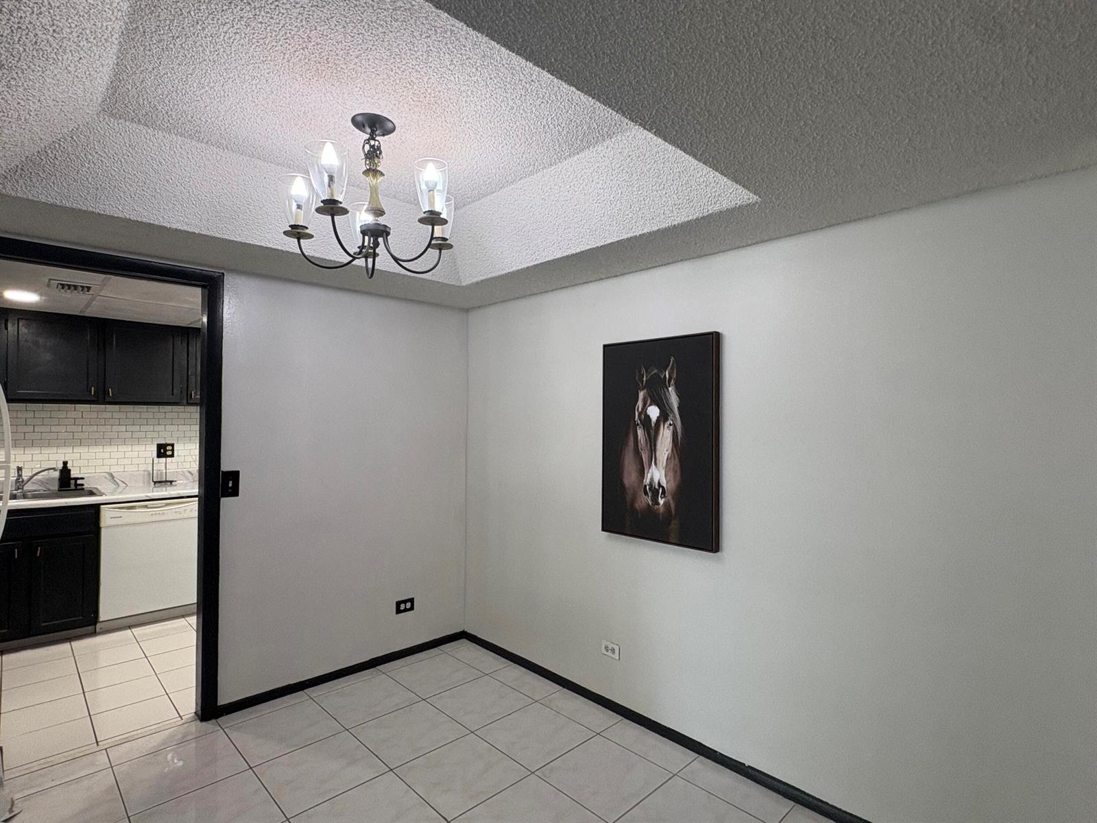 A dining area features a tray ceiling with a chandelier, white walls, and tile flooring — 3660 Inverrary Drive # 1b, Lauderhill FL 33319, LAUDERHILL, FL