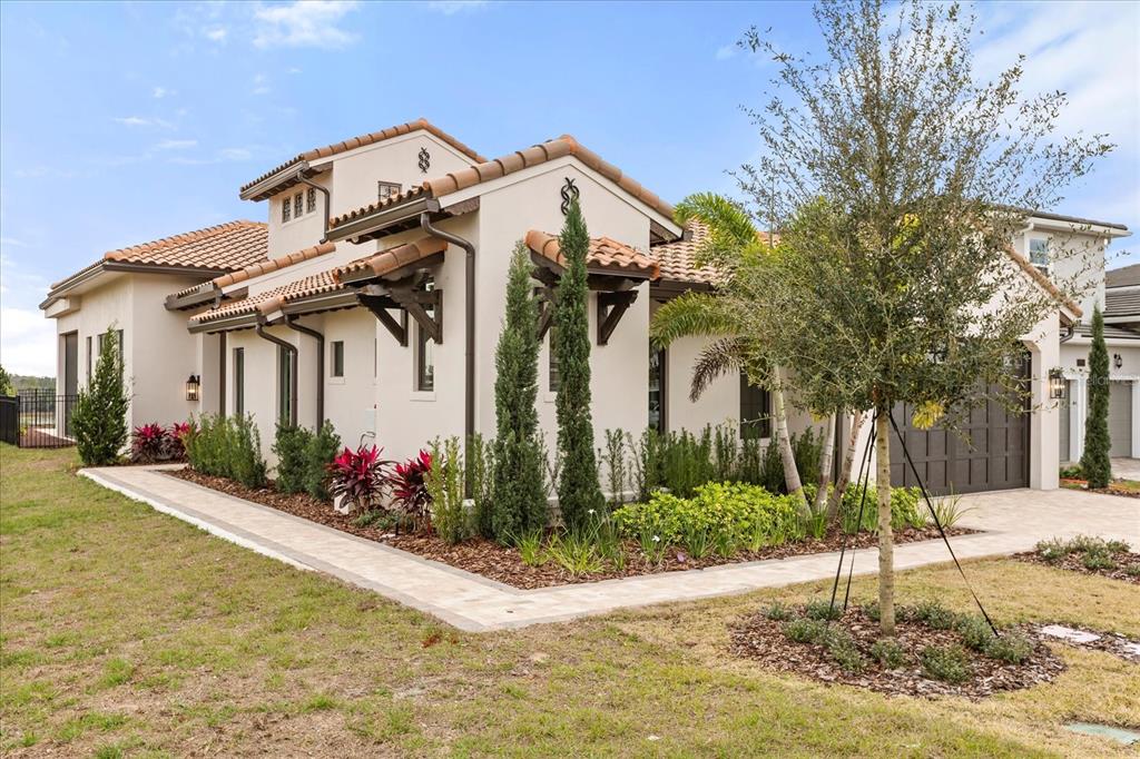 A side view of a beige stucco house with a tile roof and landscaped yard — 16001 VOLTERRA POINT, BELLA COLLINA, FL