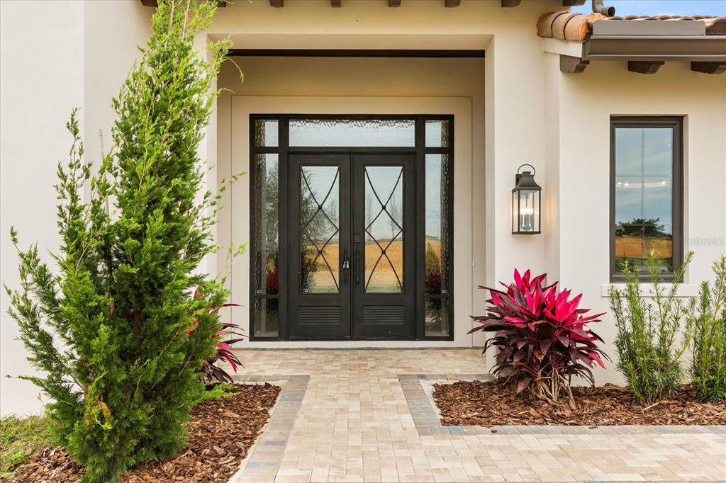 A front entryway features double glass doors with iron accents, a lantern light, and landscaping — 16001 VOLTERRA POINT, BELLA COLLINA, FL