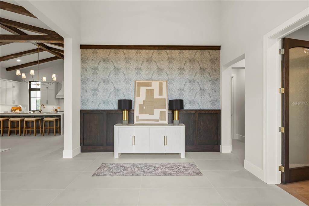 A foyer features a white console table, dark wood wainscoting, and patterned wallpaper — 16001 VOLTERRA POINT, BELLA COLLINA, FL