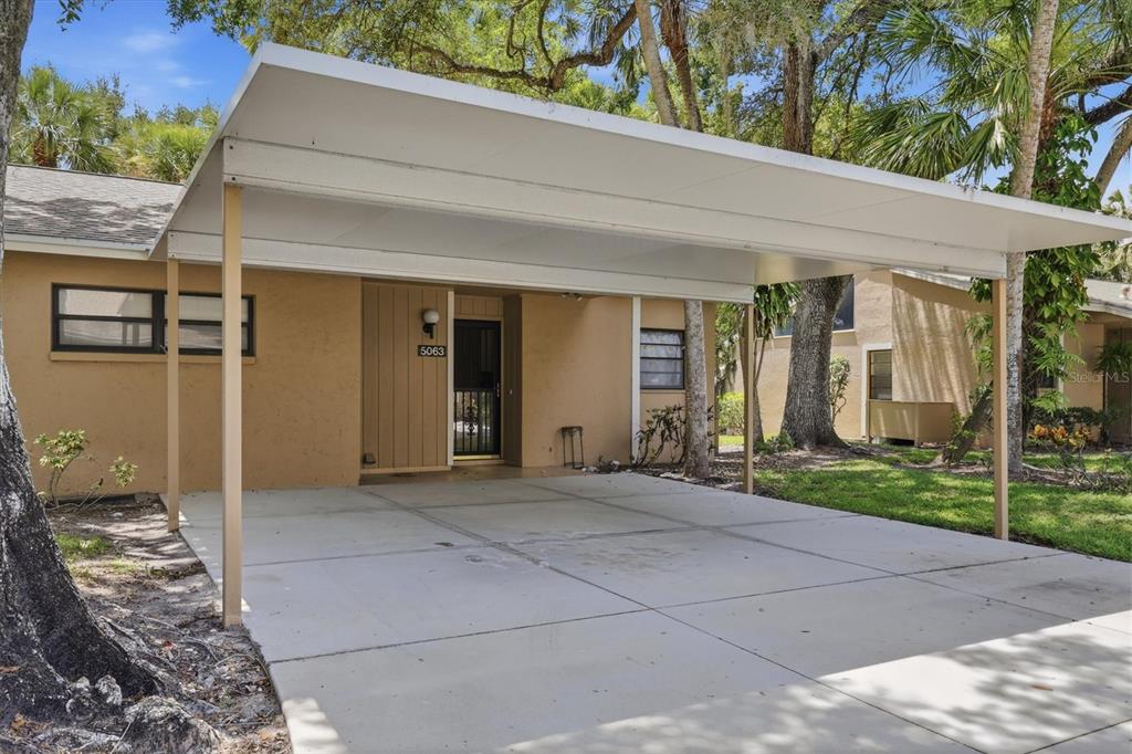 A tan house exterior features a large concrete carport and a front entrance door — 5063 VILLAGE GARDENS DRIVE UNIT 9, SARASOTA, FL
