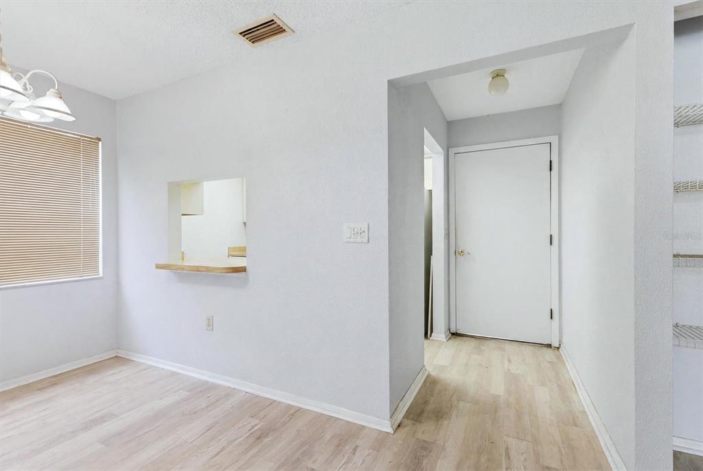 A dining area with light wood-look flooring, a pass-through window, and a white door — 5063 VILLAGE GARDENS DRIVE UNIT 9, SARASOTA, FL