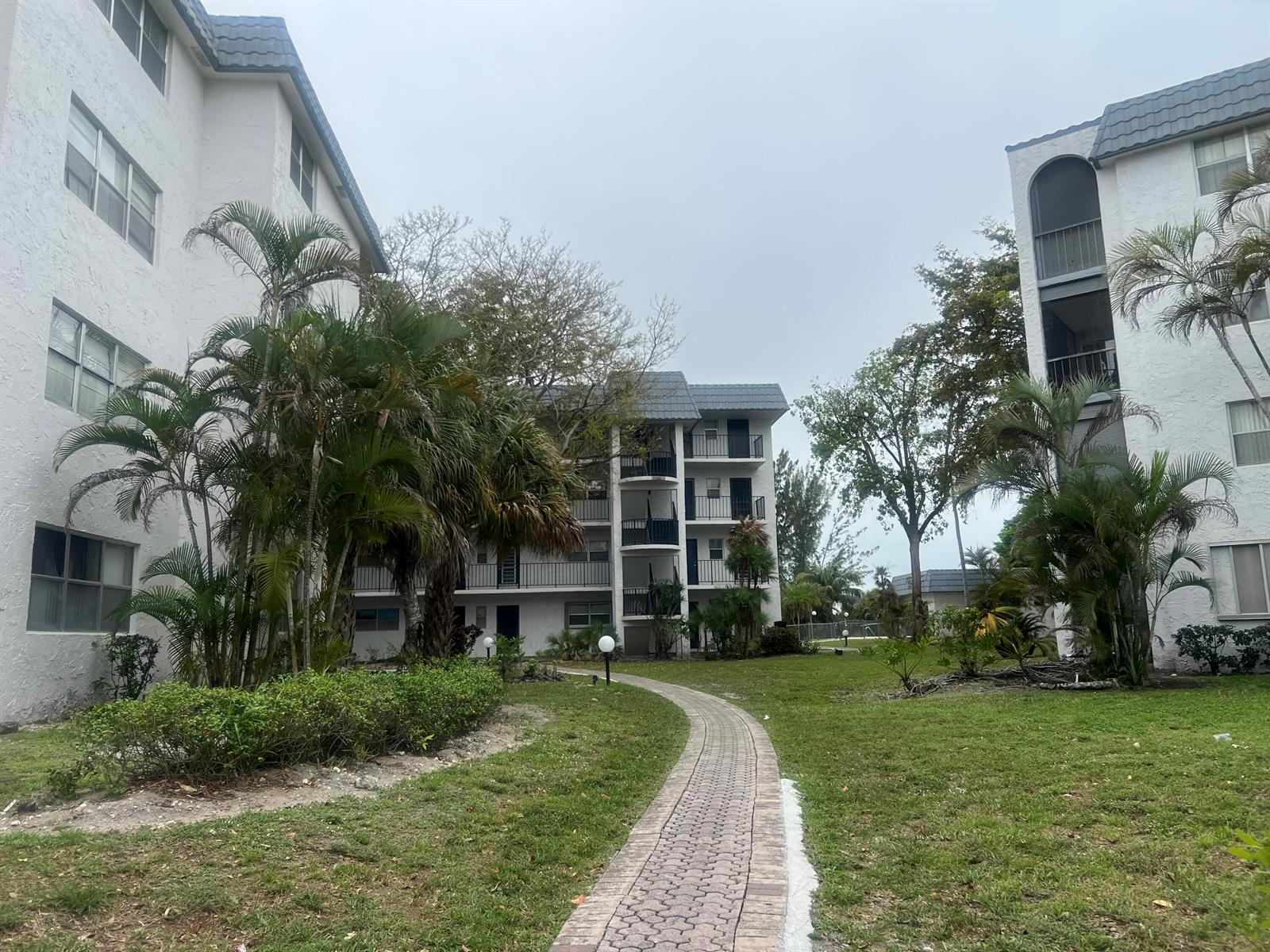 A paved walkway leads between two multi-story apartment buildings surrounded by palm trees and grass — 3300 Spanish Moss Terrace # 111, Lauderhill FL 33319, LAUDERHILL, FL