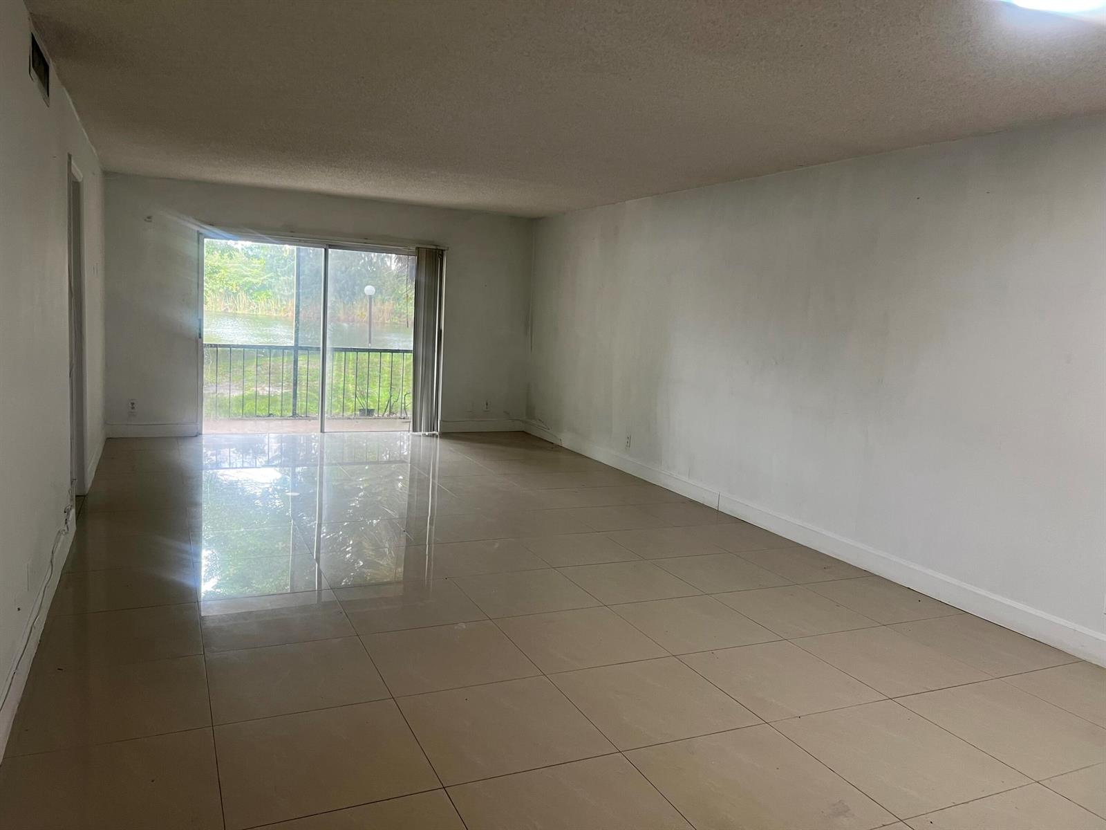 An empty living room with large beige floor tiles, white walls, and a sliding glass door — 3300 Spanish Moss Terrace # 111, Lauderhill FL 33319, LAUDERHILL, FL