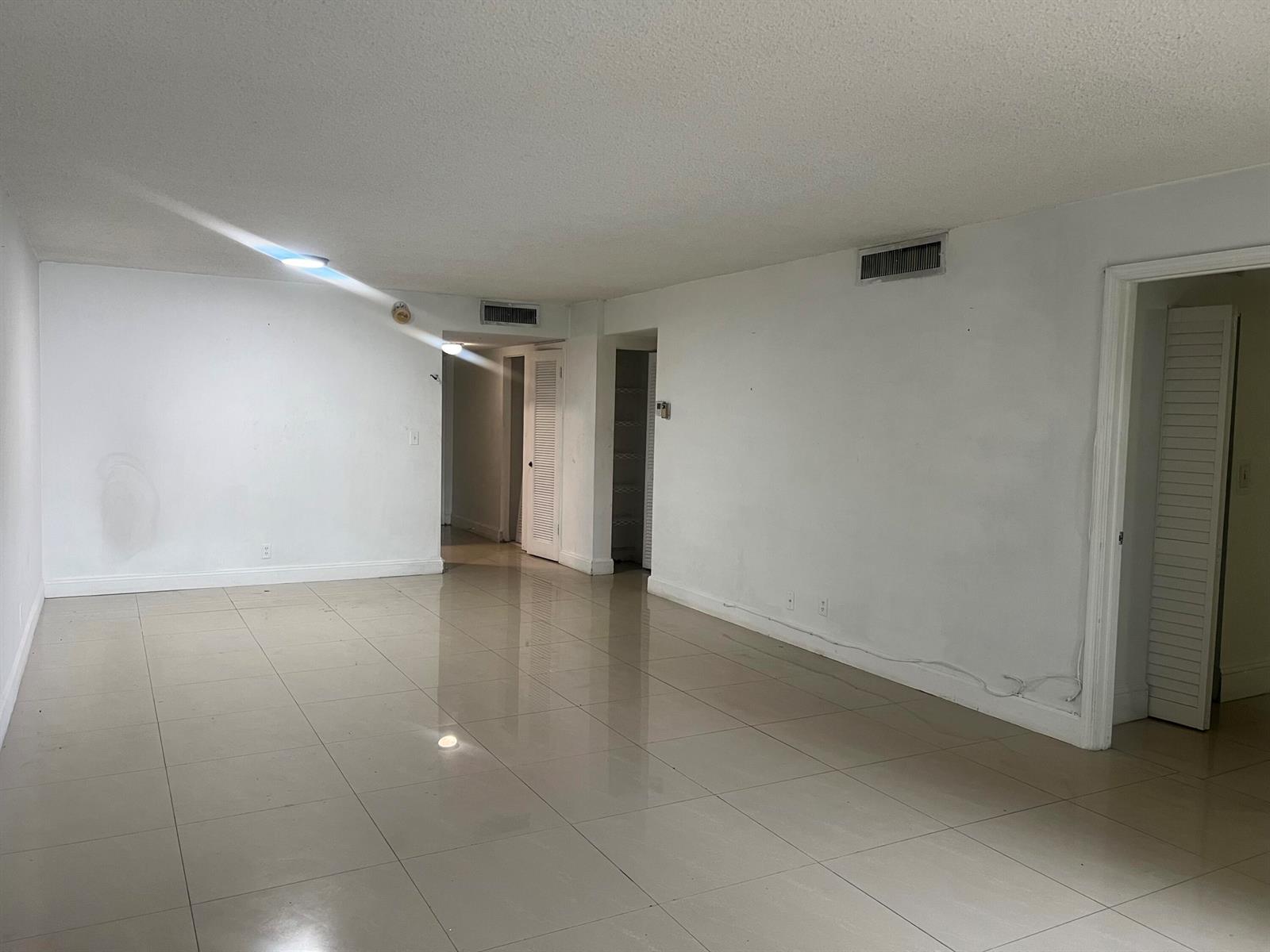 An empty room with white walls, beige tile flooring, and several doorways with louvered doors — 3300 Spanish Moss Terrace # 111, Lauderhill FL 33319, LAUDERHILL, FL