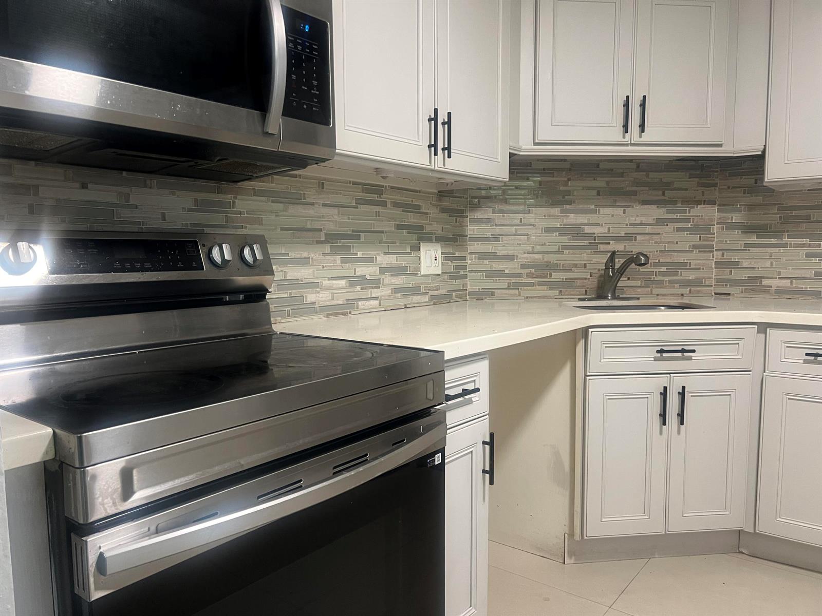 A kitchen features white cabinets, stainless steel appliances, a tiled backsplash, and a corner sink — 3300 Spanish Moss Terrace # 111, Lauderhill FL 33319, LAUDERHILL, FL
