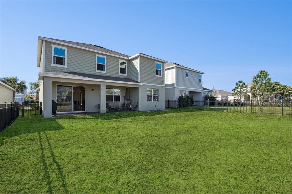 The exterior rear view of a two-story house features a covered patio and fenced yard — 609 FORTUNA DRIVE, DAVENPORT, FL