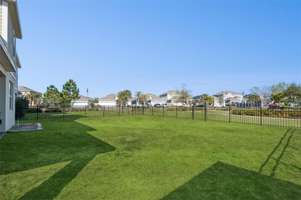 A grassy backyard features a black metal fence and a view of neighboring houses — 609 FORTUNA DRIVE, DAVENPORT, FL