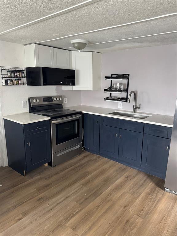 A kitchen features dark blue lower cabinets, white upper cabinets, stainless steel appliances, and wood flooring — 9204 66TH STREET NORTH, PINELLAS PARK, FL