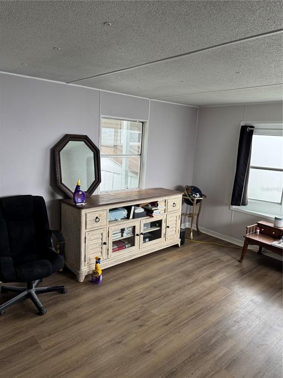 A room with light-colored walls, wood-look flooring, a wooden media console, and a black chair — 9204 66TH STREET NORTH, PINELLAS PARK, FL
