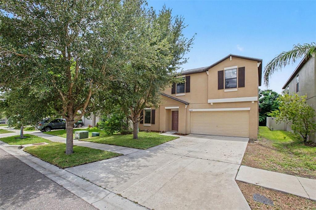 A two-story tan house with a two-car garage and a front yard with trees — 10138 ROSE PETAL PLACE, RIVERVIEW, FL