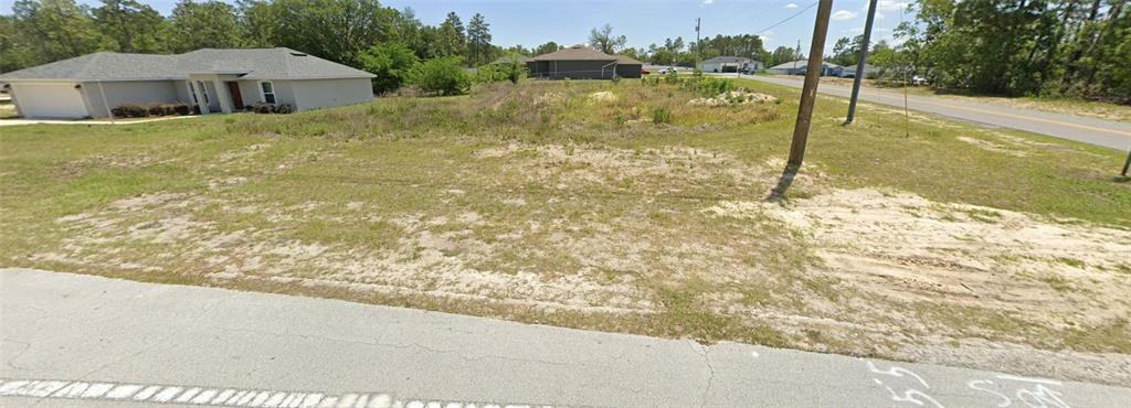 A vacant, grassy residential lot sits next to a single-story house along a paved road — LOT 29 MARION OAKS TRAIL, OCALA, FL