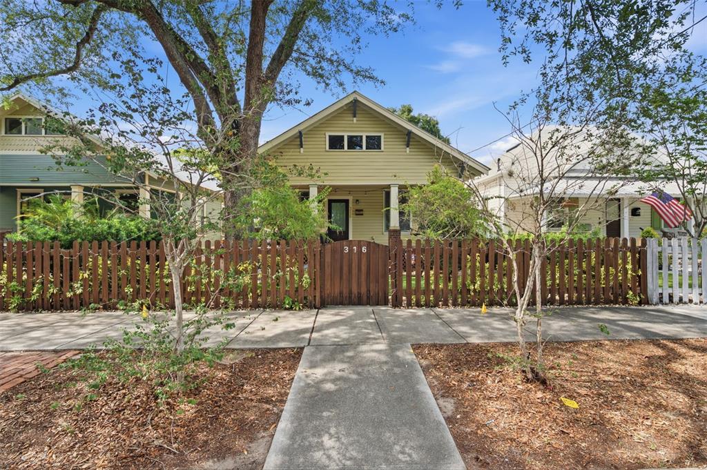 A single-story house with light green siding and a wooden fence stands behind a sidewalk — 316 E FRANCES AVENUE, TAMPA, FL