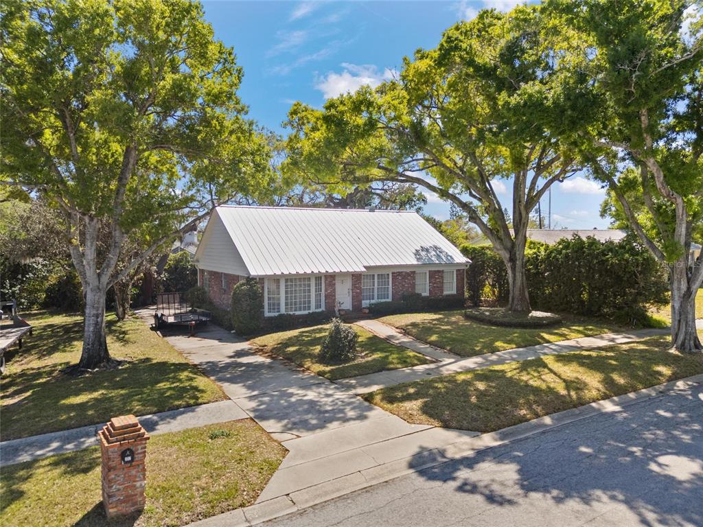 A single-story brick house with a white metal roof sits on a tree-lined lot — 502 HILLCREST AVENUE, TARPON SPRINGS, FL