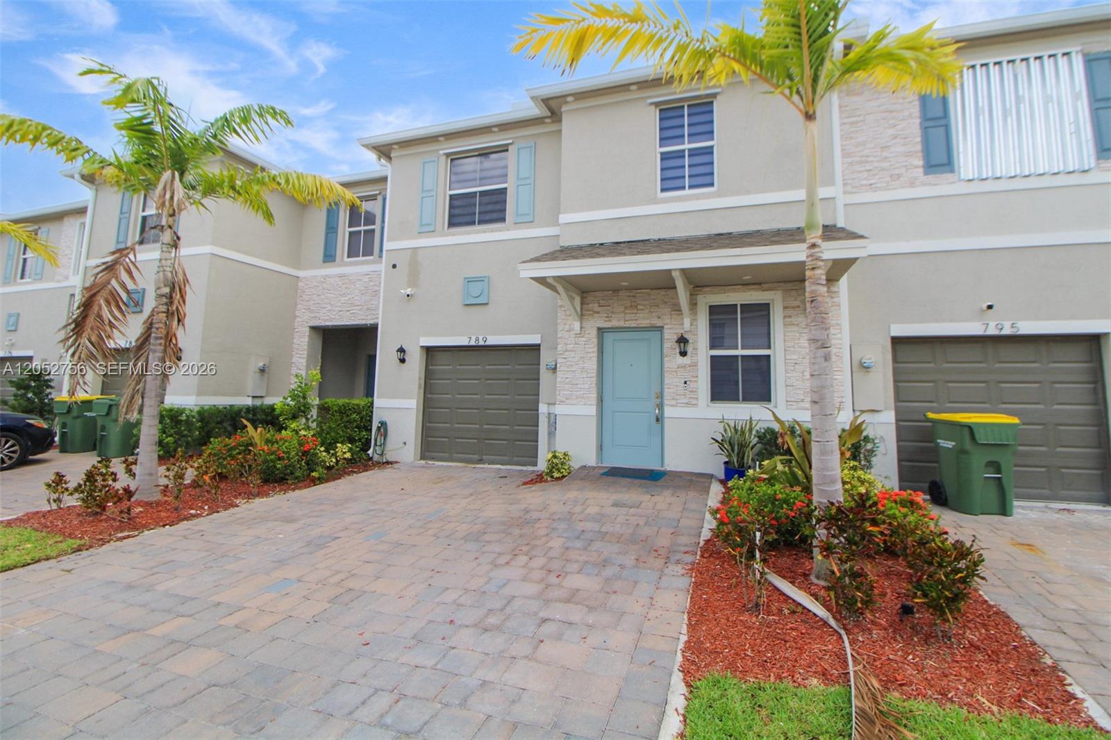 A two-story townhouse exterior features a paved driveway, a light blue front door, and palm trees — 789 SE 16th Ct, Homestead FL 33034, HOMESTEAD, FL