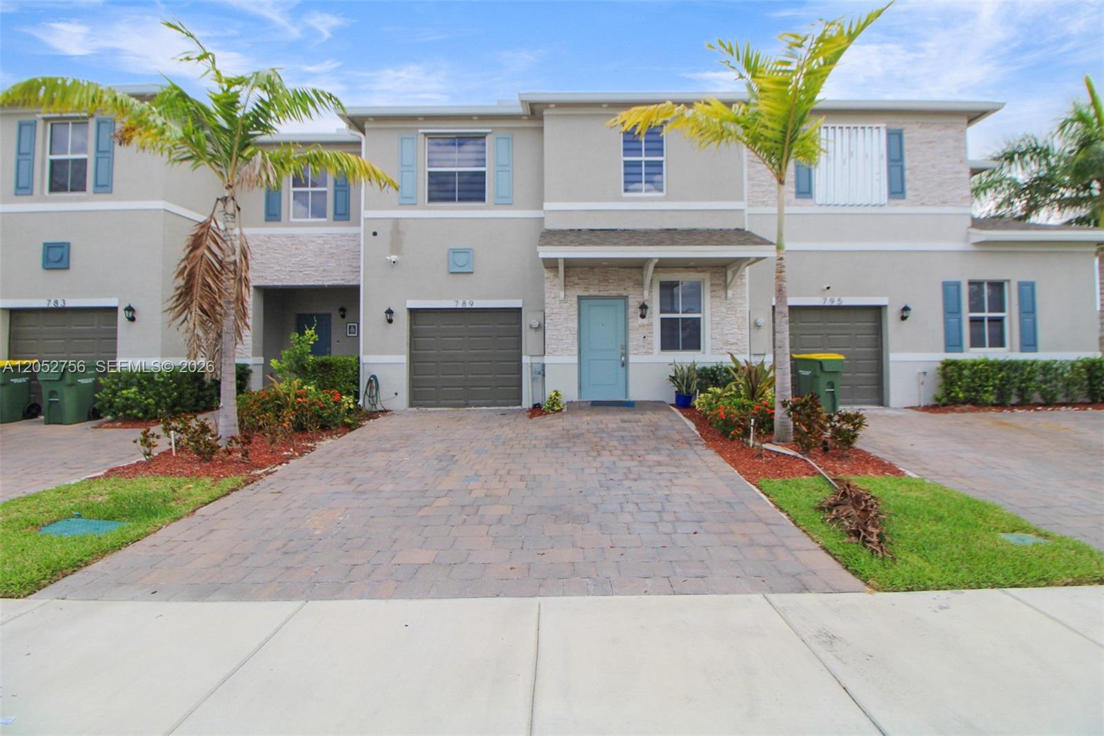 A two-story townhouse exterior features a paved driveway, a garage, and a light blue door — 789 SE 16th Ct, Homestead FL 33034, HOMESTEAD, FL