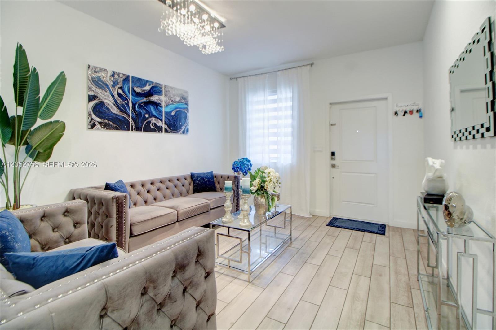 A living room features a tufted gray sofa, glass coffee table, and blue wall art — 789 SE 16th Ct, Homestead FL 33034, HOMESTEAD, FL