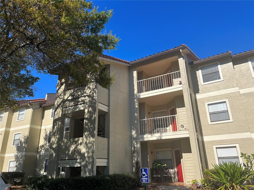 A three-story apartment building exterior features tan stucco walls, balconies, and a handicap parking sign — 3016 PARKWAY BOULEVARD UNIT 209, KISSIMMEE, FL